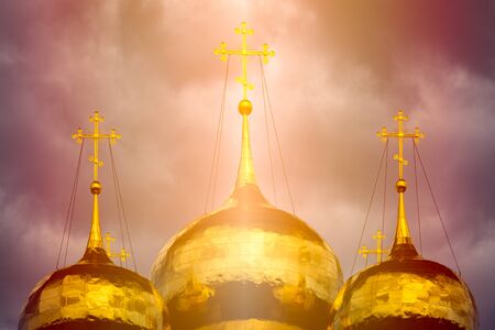 Onion dome of traditional russian church. Golden cupola with crosses, sun shining and dramatic sky in background.の写真素材