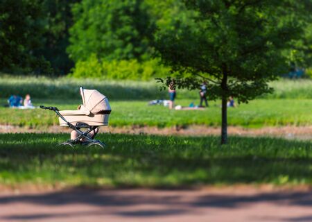 Baby carriage in park with parent nearby. People relax in city green zone.の写真素材