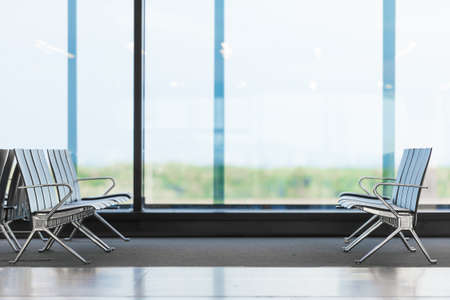 Empty rows of seats in airport waiting area. Chairs in big light hall waiting for passengers to arrive. Trips and travelling. Airfield in backgroundの写真素材
