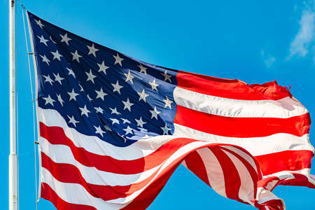 US american flag and blue cloudy sky with clouds in backgroundの写真素材