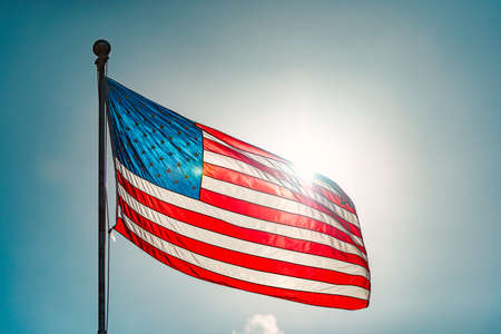 US american flag and blue cloudy sky with clouds in backgroundの写真素材