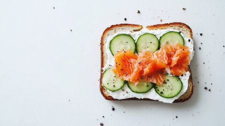 Healthy open-faced sandwich with cream cheese, salmon, and cucumber slices, styled on a minimalist white surfaceの素材