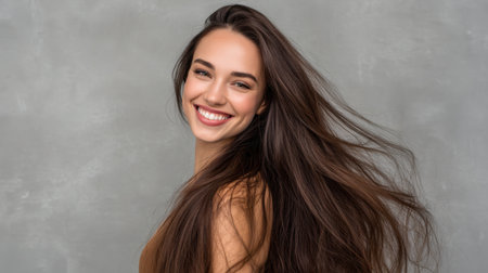 A cheerful young woman with long hair smiles radiantly, embodying joy and natural beauty against a soft gray backdrop. Perfect for lifestyle themes.の素材