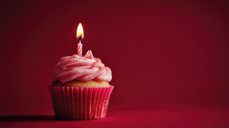 Pink frosted cupcake with a lit candle, highlighted against a deep red background. The image captures the essence of celebration and joy.の素材