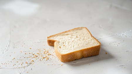 A piece of bread, fallen and lying on the white floor, emphasizing the moment of its unexpected drop.の素材
