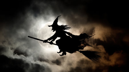 A captivating silhouette of a witch soaring on her broomstick, framed by an enchanting full moon and turbulent clouds, perfect for Halloween or fantasy themes.の素材
