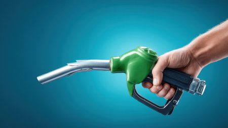 Close-up image of a hand gripping a fuel dispenser nozzle against a vibrant blue background, symbolizing energy, transportation, and the modern automotive industry.の素材