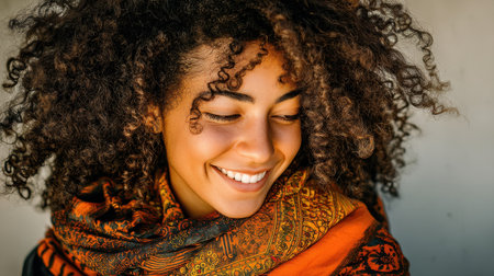 This portrait captures a joyful young woman smiling with curly hair, dressed in a vibrant scarf. The image radiates positivity and warmth, perfect for lifestyle themes.の素材
