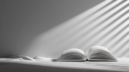 An open book rests on a smooth white surface, softly illuminated by gentle sunlight rays, evoking feelings of calm and inspiration in a minimalist setting.の素材