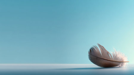A delicate feather rests elegantly on a smooth surface against a soft blue background, evoking feelings of lightness, calm, and serenity. Perfect for design themes.の素材