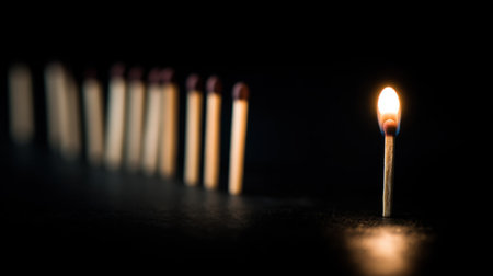 A close-up view of a lit match with a vibrant flame in focus, surrounded by a line of unlit matches against a dark backdrop.の素材