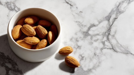 A beautifully arranged bowl of almonds sits on a marble countertop, illuminated by soft sunlight, creating an inviting and healthy food scene.の素材