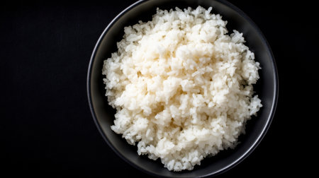 A close-up view of freshly cooked and fluffy white rice served in a dark bowl, creating a simple yet elegant presentation against a black background.の素材
