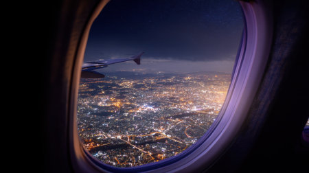 This breathtaking image captures a vibrant city skyline at night from an airplane window, showcasing twinkling lights and atmospheric views.の素材