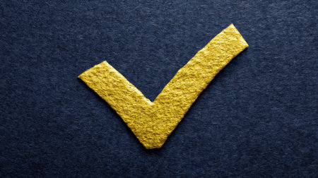 A vibrant yellow check mark crafted from textured paper stands out against a dark blue background, symbolizing approval and success.の素材