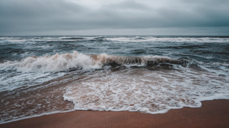This captivating image captures the gentle waves washing ashore on a sandy beach, under a moody, cloudy sky, evoking tranquility and calmness.の素材