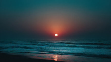 A tranquil sunset paints the sky in beautiful hues as the sun sets over calm ocean waves, casting a soft reflection on the sandy beach.の素材