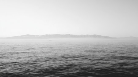 A tranquil black and white seascape featuring gentle waves under an overcast sky. The misty horizon reveals distant mountains, creating a serene atmosphere perfect for relaxation and meditation.の素材