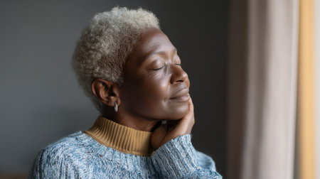 A serene, mature African American woman with short gray hair radiates calmness as she relaxes by the window. She embodies tranquility and self-care.の素材