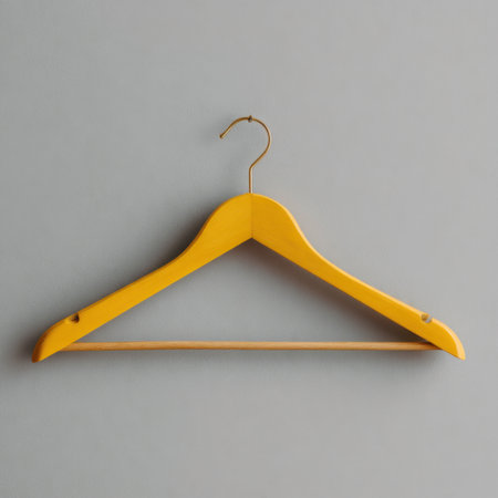 A vibrant yellow wooden hanger hangs against a subtle gray wall, showcasing a minimalist yet stylish accessory for fashion displays and home decor.の素材