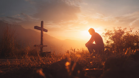 A solitary figure kneels in reflection beside a cross at sunset, embodying themes of spirituality and peaceful contemplation in a beautiful natural setting.の素材