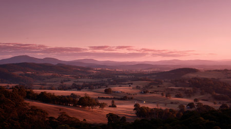 Experience the serene beauty of a tranquil dawn in this breathtaking landscape, showcasing rolling hills and a soft pink sky illuminating glistening fields.の素材