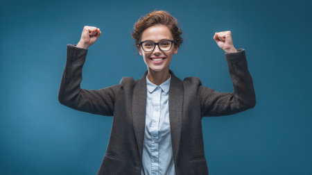 A cheerful young woman celebrates her success with raised fists, illustrating confidence and joy. The vibrant background enhances her positive energy and motivation, perfect for themes of achievement and empowerment in lifestyle photography.の素材
