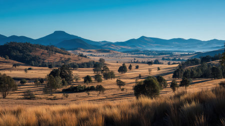 A stunning landscape showcasing rolling hills adorned with lush trees under a clear blue sky, capturing the beauty of nature in serene early morning light.の素材