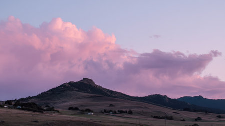 Captivating view of a mountain range under a vibrant twilight sky with soft pink clouds illuminating the tranquil landscape below.の素材