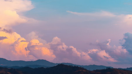 A breathtaking view of a vibrant sunset highlighting rolling mountains beneath a sky filled with soft clouds in pastel tones.の素材