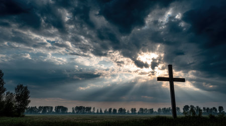A stunning landscape features a wooden cross silhouetted against dramatic clouds with rays of light piercing through the sky, creating a serene atmosphere.の素材