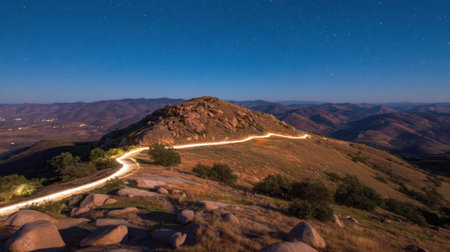 A captivating view of a winding road leading through rocky hills at night, showcasing a serene landscape under a beautifully starry sky.の素材