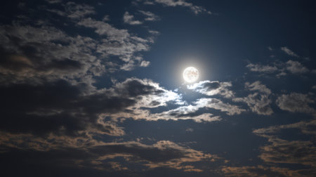 A stunning full moon shines brightly in a dark blue night sky, surrounded by wispy clouds, creating a serene and mystical atmosphere.の素材