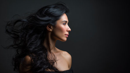 A captivating profile shot of a young woman with long, flowing dark hair, set against a soft black background that emphasizes her beauty and grace.の素材