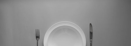 The concept of gastronomy and food. View from above of an empty white plate with fork and knife against a gray background. Serving dinner in a restaurant.の写真素材