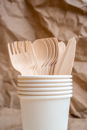 Cardboard cups, wooden forks and spoons against a background of crumpled kraft paper. A simple,...