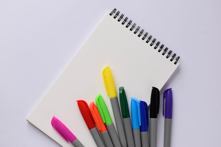A blank notepad and colored felt-tip pens on a white background. Multicolored felt-tip pens for...