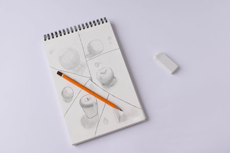 Top view of an open spiral blank notebook with a drawing and wooden pencil on a white tabletop background.の写真素材
