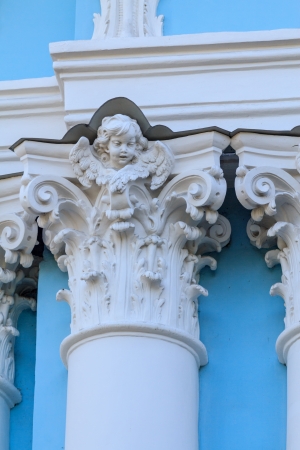 A white corinthian column with an angel face and wings on a light blue wallの写真素材