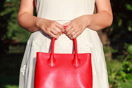 A newly engaged woman holding a red expensive leather bag showing her engagement ringの写真素材