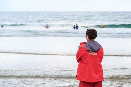 A beach lifeguard in a red jacket on hot water beach in New Zealand