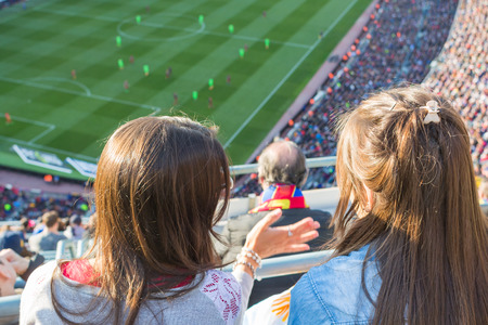 Two girls watching a football game in a large stadiumの写真素材