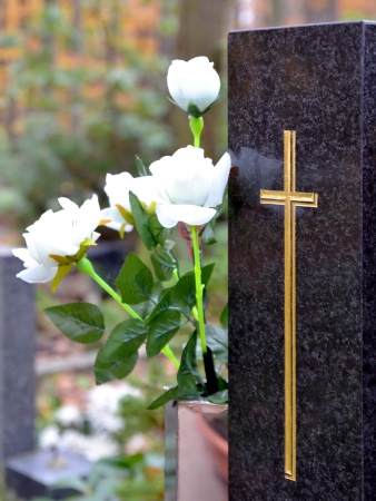 Tombstone with golden cross and white roses at cemeteryの写真素材