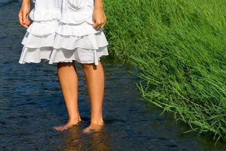 Pretty woman's legs  cooling in the fresh stream near the green grassの写真素材