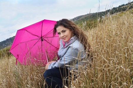 Beautiful calm lady with pink umbrella resting in autumn grassの写真素材