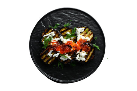 Grilled eggplant with red caviar and feta cheese on black plate isolated on white backgroundの写真素材