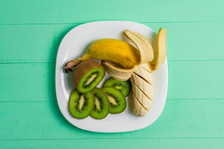 Ripe banana, pear and slice kiwi on a white plate on wooden vintage backgroundの写真素材