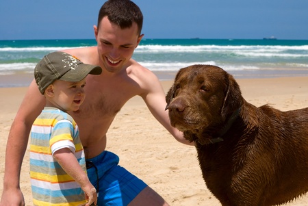 Happy father and son playing on beach with dogの写真素材