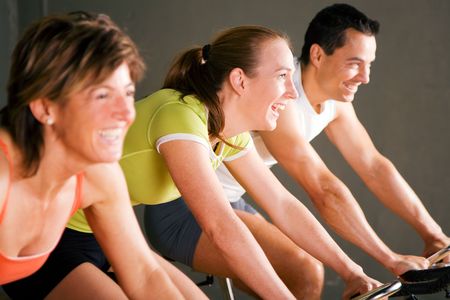 Tree people spinning on stationary bicycles in a gym or fitness club; focus on girl in the middle