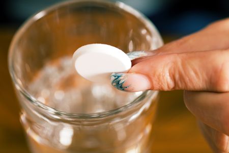 Hand holding a pill over a glass of water (macro)の写真素材